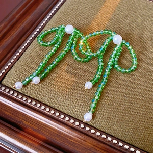Detail of crystal bow earrings with green beads, pearls, and tassels on a vintage box