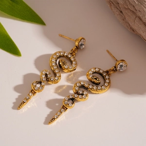 Detailed shot of golden snake stud earrings featuring sparkling rhinestones on white stone