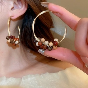 Detail view of large C-shaped twisted gold hoops with multi-color natural wooden beads