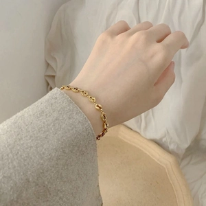 Close-up of a gold coffee bean link bracelet worn on a wrist over a minimal background