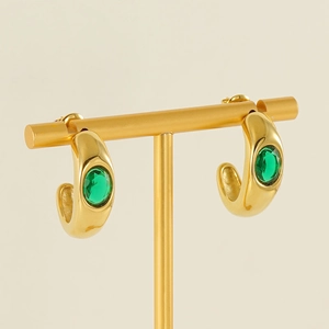 Golden C-shaped stainless steel earrings with green zircon on a jewelry stand