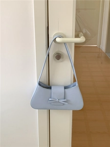 Close-up of light blue baguette bag with a decorative bow hanging on a door handle