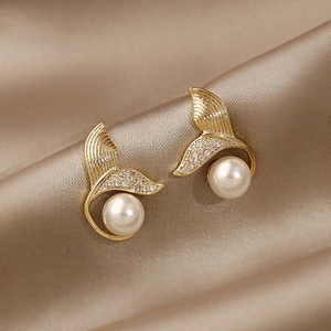 Detail of elegant gold fishtail earrings with sparkling zircons and white pearls