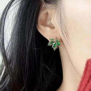 Gros plan de boucles d'oreilles feuille d'érable aux cristaux verts sur un modèle
