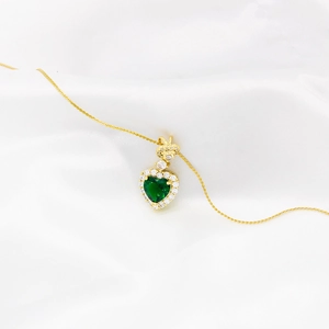 Gold heart pendant necklace with green emerald and diamonds on white silk background
