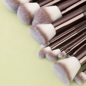 Detail of 11-piece makeup brush set with wooden handles and copper ferrules on green background