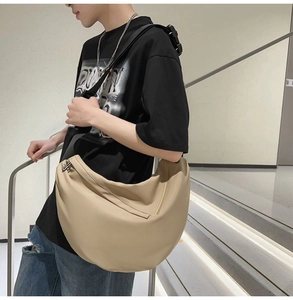 Detail of a beige crescent crossbody bag in durable nylon worn by a model on stairs