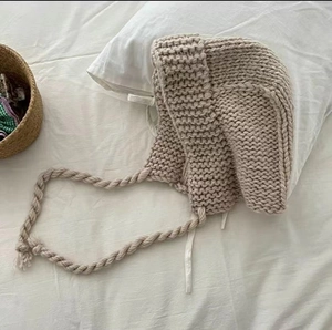 Gros plan du bonnet en maille épaisse beige avec liens tressés sur fond blanc doux