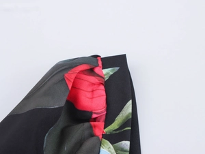 Detailed macro view of the black floral print fabric with red flowers and green leaves