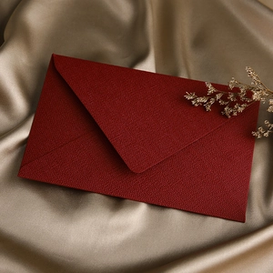 Detail of dark red textured paper envelope on champagne silk background with dried flower