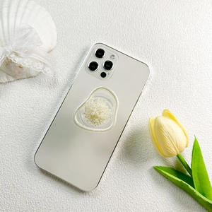 Detail view of heart-shaped pearl flower phone grip stand on a white textured background