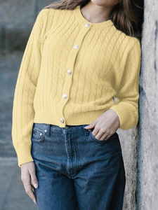 Detail of yellow cable knit cardigan with silver buttons and long sleeves in outdoor setting