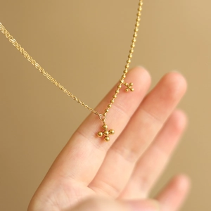 Detail of 18K gold-plated beaded cross pendant on a delicate stainless steel chain