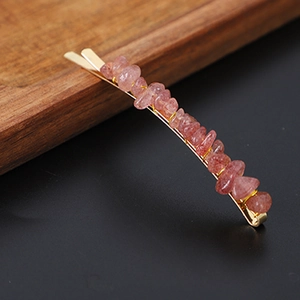 Close-up of gold hair clip featuring natural irregular pink crystal quartz stones on black background