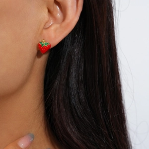 Close-up of a model wearing cute red strawberry stud earrings with gold metal base