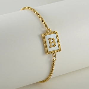 Detail of adjustable gold box chain bracelet with white shell pendant and letter B charm
