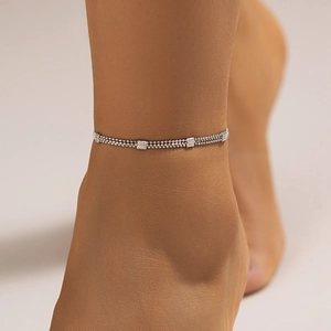 Detail view of multi-layered silver beaded ankle chain with square charms on the ankle