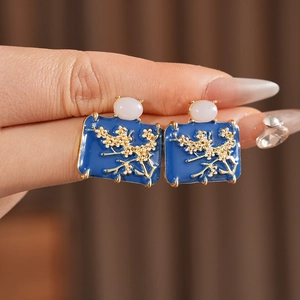 Detailed close-up of blue enamel flower earrings with gold branches and white bead