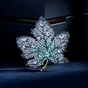 Exquisite maple leaf brooch with blue crystals and gold stem on velvet display