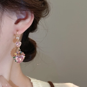 Close-up of dangling heart earrings with pink stones and colorful zircon on a model