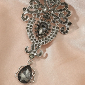 Detail of luxury crown brooch with smoky crystals and pear-shaped drop on satin