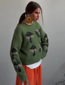 Close-up of green knit sweater showing detailed mushroom pattern and soft wool texture