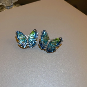 Détail de boucles d'oreilles papillon avec ailes dégradées bleu-vert et perle centrale