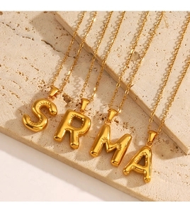 Detail of 3D balloon style gold letter pendants on fine chains over stone texture