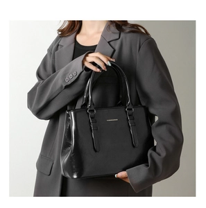 Lifestyle shot of a black glossy leather handbag styled with a formal grey business blazer
