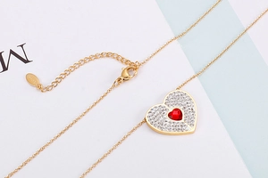 Close-up of heart-shaped gold necklace with red stone and pavé zircon settings
