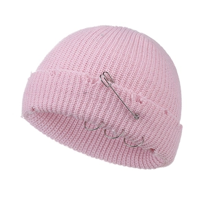 Detail of pink distressed knit beanie with metal safety pin and silver rings accessory