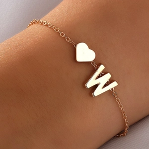 Détail d'un bracelet doré avec cœur et pendentif lettre W sur le poignet d'une femme