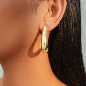 Gros plan d'une boucle d'oreille goutte dorée au fini métallique poli sur un mannequin