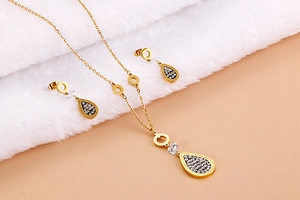 Close-up of golden leaf pendant and earrings set with zircons on white plush background