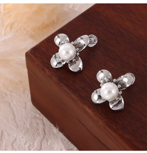 Close-up of flower-shaped silver earrings with pearl accents on a wooden box