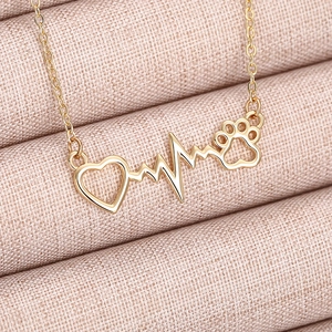 Macro shot of a golden heart and paw print necklace on soft pink fabric background
