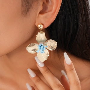 Close-up of golden vintage flower earrings with blue stamen detail worn by a model