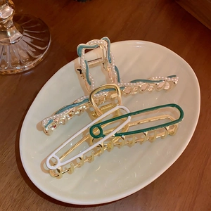 Detail view of gold alloy hair clips with dark green enamel and elegant white pearls