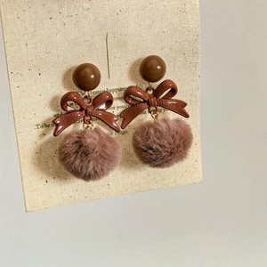 Close-up of brown bow earrings with fluffy fur balls on a beige textured jewelry card