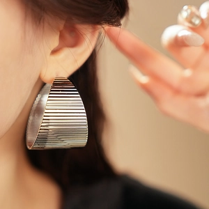 Close-up of wide silver geometric earring with textured stripes on model ear