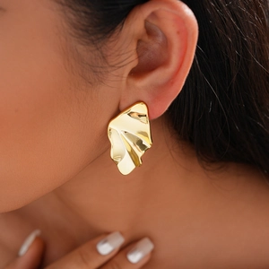 Close-up of a model wearing a gold geometric crumpled metal earring with a glossy finish