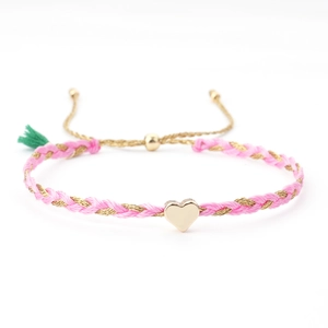 Pink and gold woven friendship bracelet with a polished heart pendant and green tassel detail