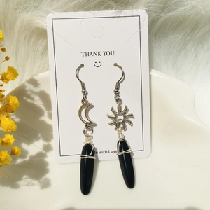 Detail of sun and moon stainless steel earrings with wire-wrapped black stone pendants