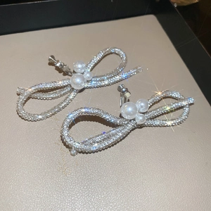Close-up of sparkling silver bow earrings with white pearl detail on a leather tray