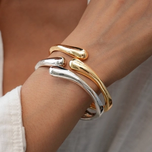 Detailed view of irregular water drop cuffs in gold and silver finish on female wrist