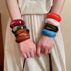 Stack of colorful thick acrylic bangles in resin finish worn on a model's wrist