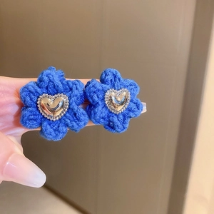 Macro shot of blue knitted flower earrings featuring silver heart metal centers