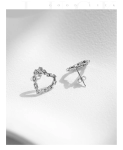 Macro shot of silver heart stud earrings with detailed geometric chain link texture