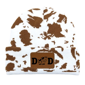 Close-up of brown and white cow pattern knitted beanie with a vintage leather DAD patch