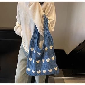 Primer plano del bolso de punto azul con patrones de corazones blancos al hombro